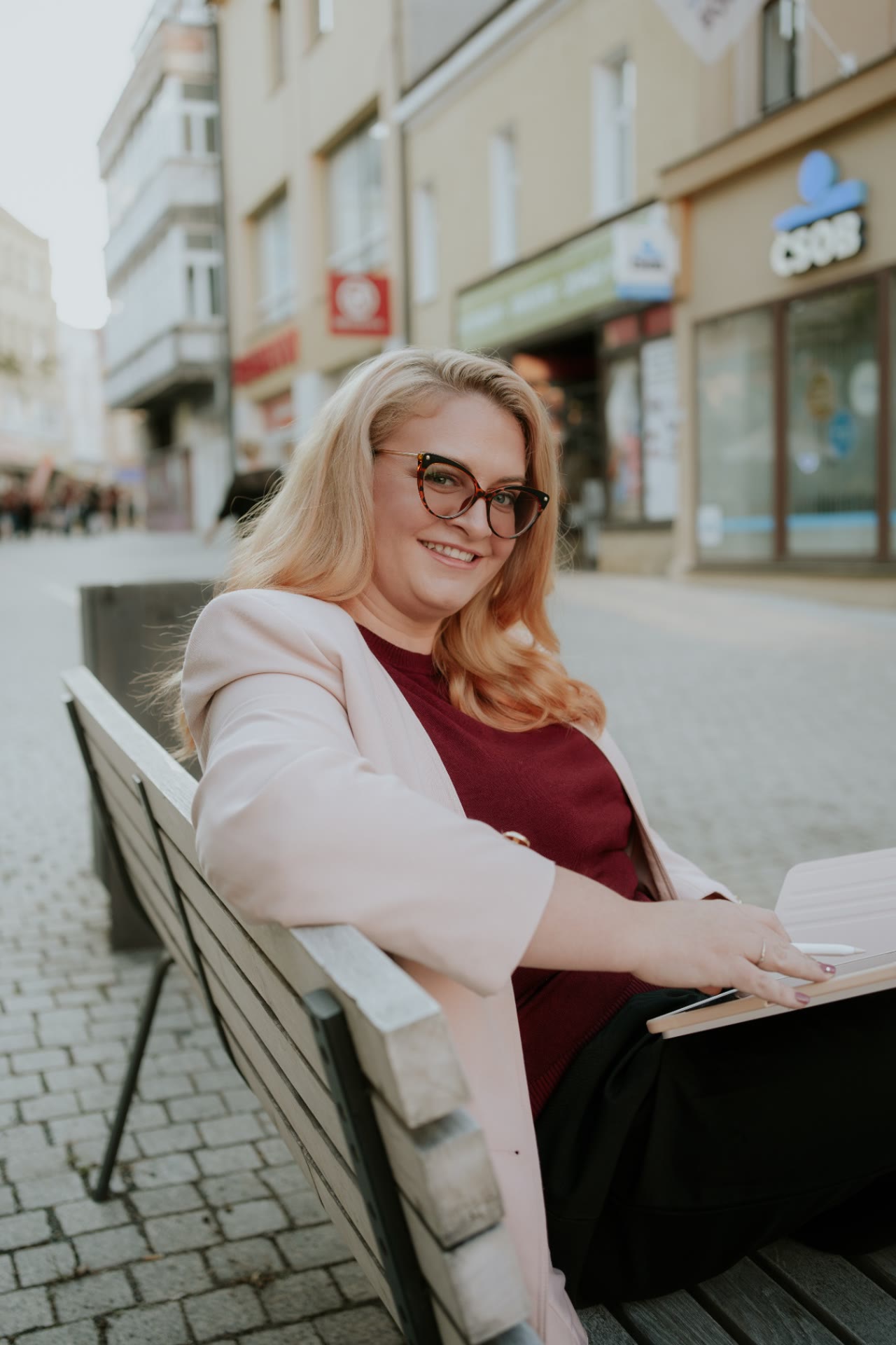 Katka Géringová pracuje na notebooku na lavičce v ulici